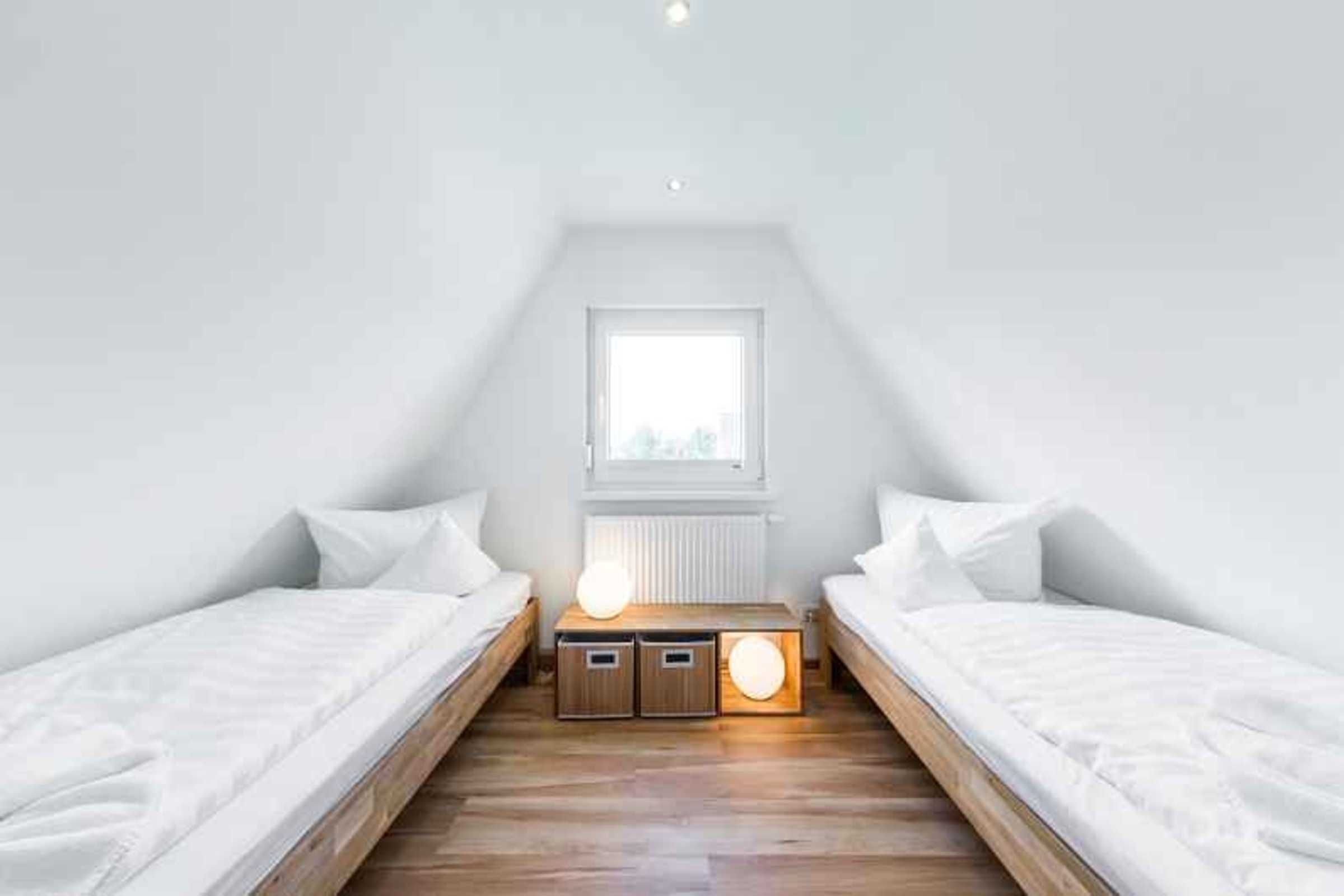 Ein kleines, gut beleuchtetes Schlafzimmer im Dachgeschoss mit zwei Einzelbetten, einem Fenster und einem Nachttisch mit Lampe.