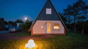 Une maison triangulaire avec une façade en briques, une petite fenêtre et une porte.