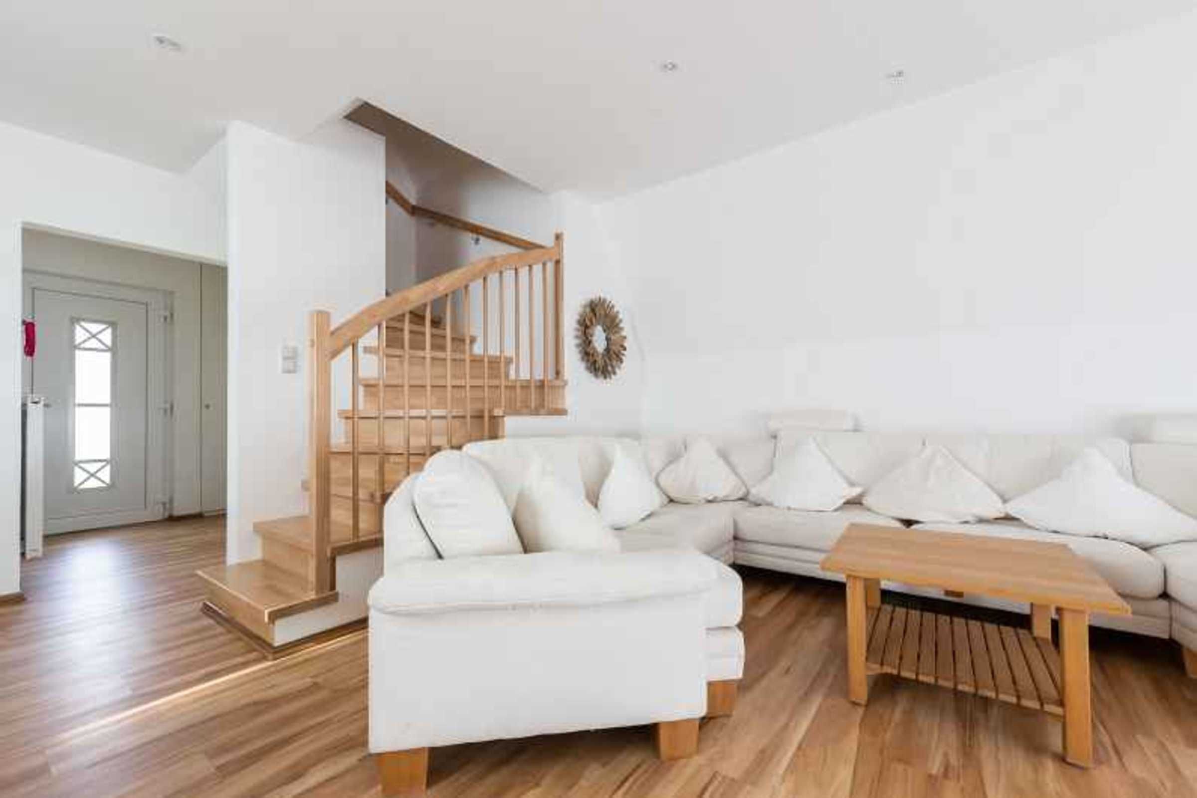A modern living room with a wooden staircase, a white sofa, and a wooden coffee table.
