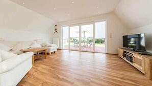 Un salon spacieux avec un canapé blanc, une table basse en bois et un téléviseur posé sur un meuble en bois.
