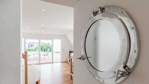 Un intérieur moderne avec un grand miroir rond au mur, un plancher en bois et une vue sur un espace extérieur aménagé avec une table et des chaises.