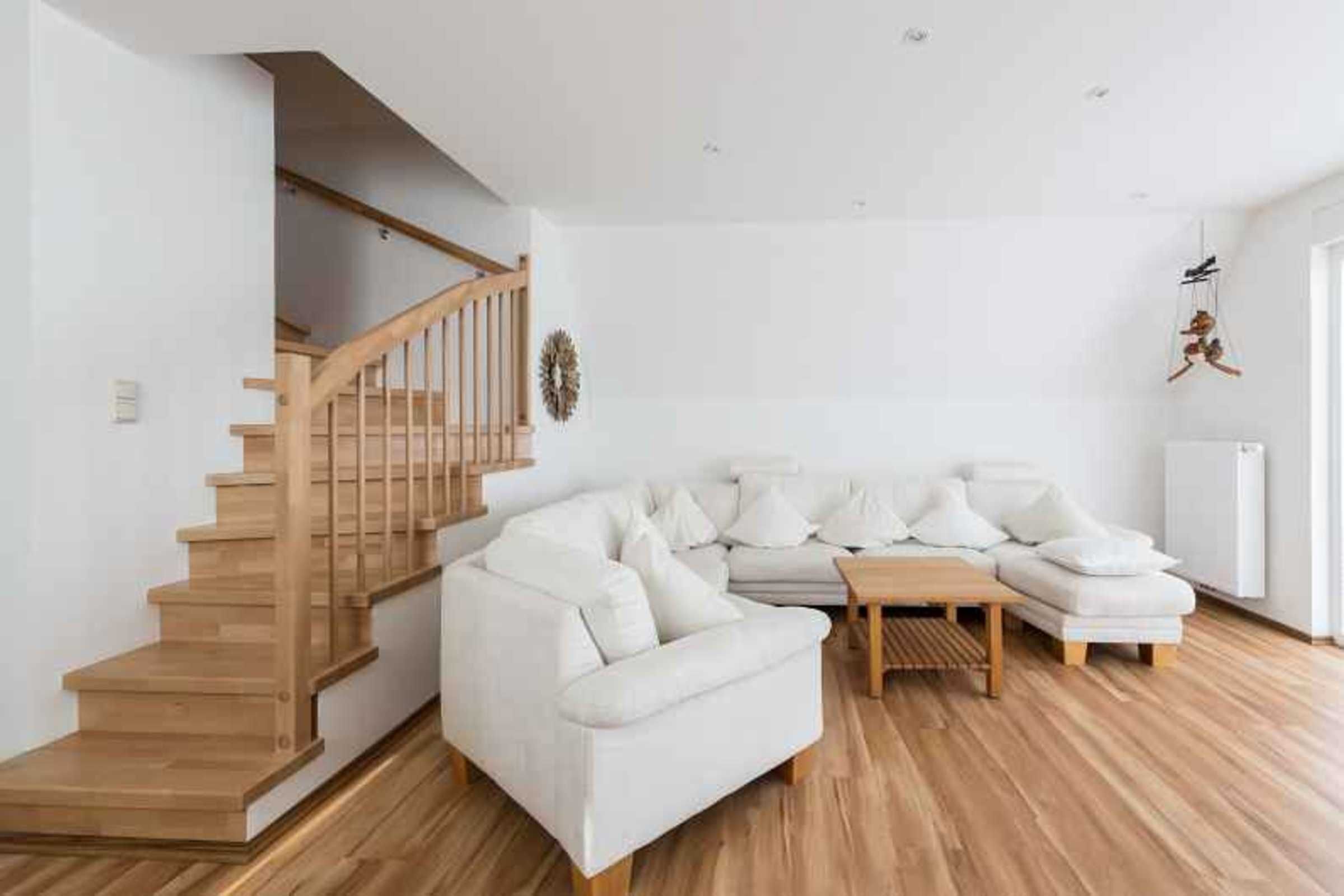Una sala de estar moderna con una escalera de madera, un sofá blanco y una pequeña mesa de madera.