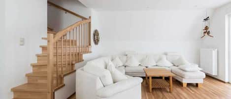 Una sala de estar moderna con una escalera de madera, un sofá blanco y una pequeña mesa de madera.