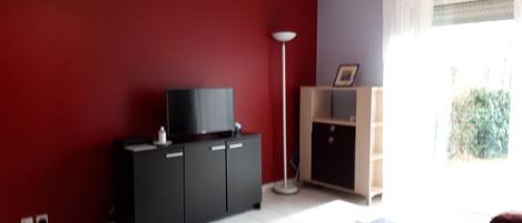 Un salon avec un mur rouge, un meuble de télévision noir, une lampe sur pied et un buffet en bois.