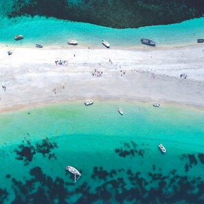 Vista aérea de una playa con barcos, gente y aguas turquesas cristalinas.