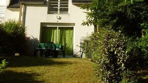 A two-story house with a garage door, a small patio with a table and chairs, and a lawn. - House (53m2) for vacations by the sea (La Forêt-Fouesnant)