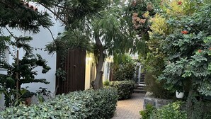 Un sendero pavimentado bordeado por abundante vegetación y una valla de madera.