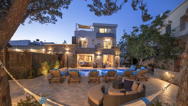 Una casa moderna de dos pisos con piscina, mobiliario exterior y una hamaca.