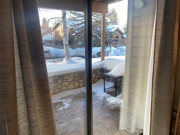 A view through a glass door to a patio with a stone wall, a metal table, and snow-covered ground.