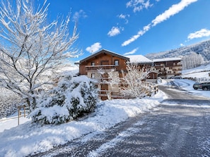 Eine Holzhütte mit Balkon, umgeben von schneebedeckten Bäumen und einem klaren Himmel.