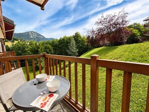 A balcony with a table set for two, overlooking a grassy hillside and a mountain.