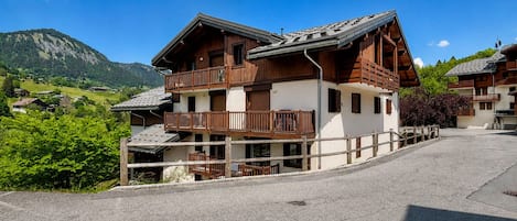 A multi-story wooden building with balconies, set against a mountainous backdrop.