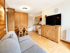 A modern living room with a sofa, wooden cabinets, a television, and a dining area with chairs and a table.