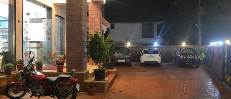 Uma motocicleta estacionada em frente a um edifício com calçada pavimentada e vasos de plantas.