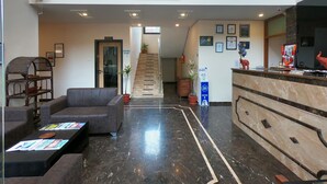 A hotel lobby with a reception desk, seating area, staircase, and a TV mounted on the wall.