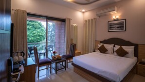 A hotel room with a bed, a desk with a chair, a small table with a basket, and a view of greenery through the window.