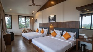 A hotel room with two beds, a desk, a chair, a ceiling fan, and large windows.