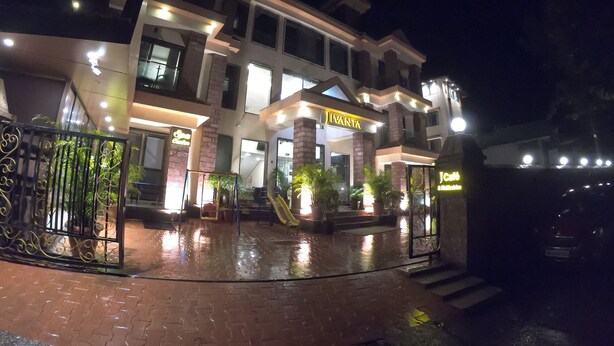 A multi-story hotel with a well-lit entrance, a gated driveway, and potted plants.