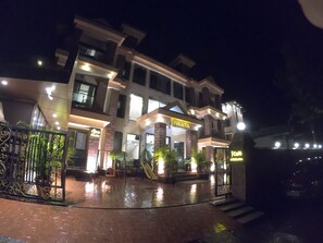 A multi-story hotel with a well-lit entrance, a gated driveway, and potted plants. - Jivanta Hotel Mahabaleshwar (Mahabaleshwar)