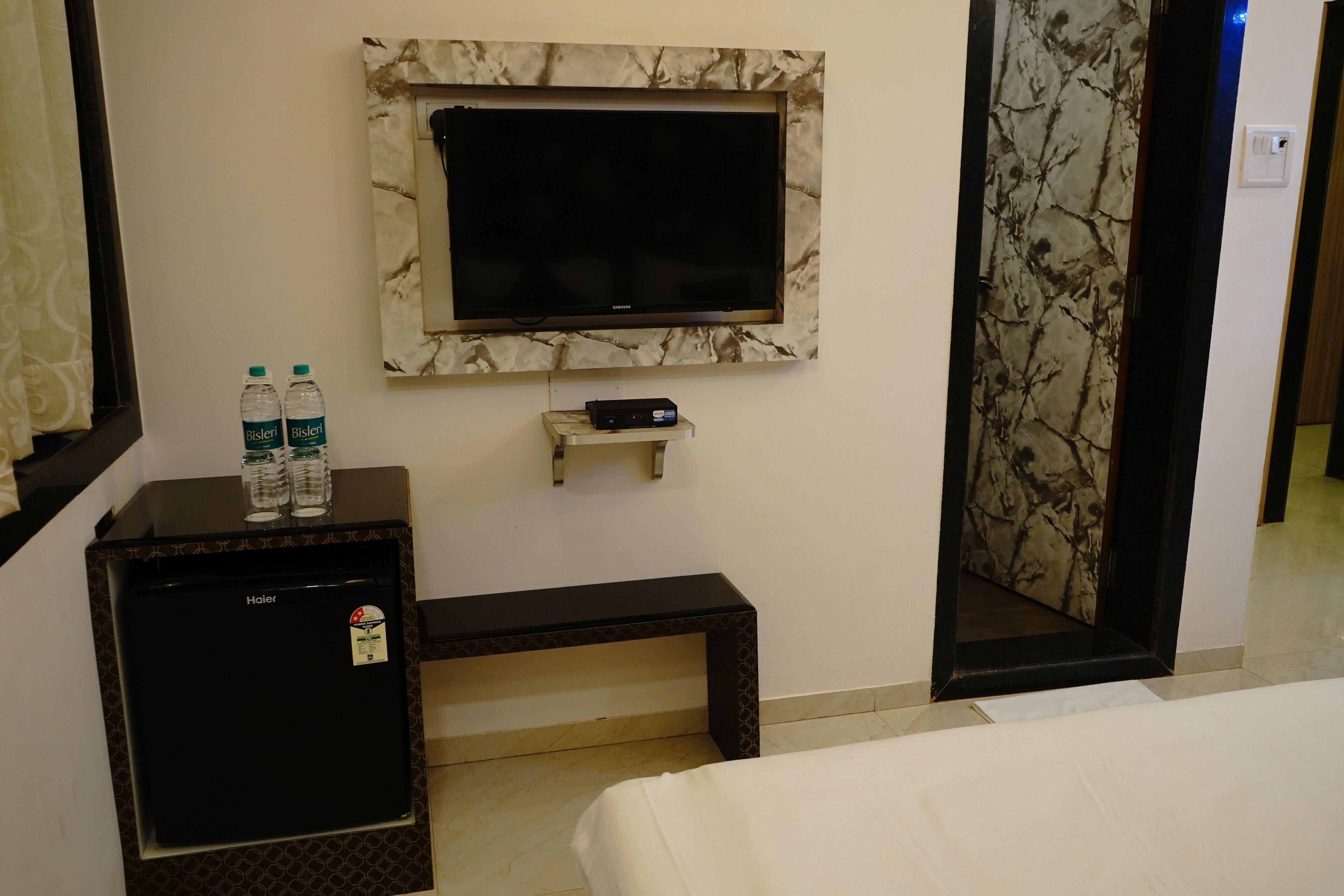 A hotel room with a bed, a small desk with a TV, a mini-fridge, and a water dispenser.