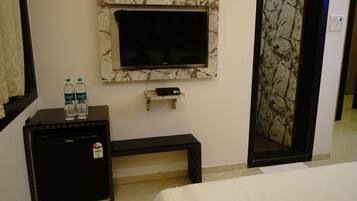 A hotel room with a bed, a small desk with a TV, a mini-fridge, and a water dispenser.