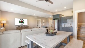 A modern living room with a sofa, a dining table, and a kitchen area with cabinets and a refrigerator. - Luxury 7BR Reunion Lodge on Thousand Hills Golf Course | Sleeps 22 | Near Highway 76 (Branson)