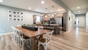 A modern kitchen with a wooden dining table, white chairs, and a kitchen island. - Luxury 7BR Reunion Lodge on Thousand Hills Golf Course | Sleeps 22 | Near Highway 76 (Branson)