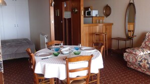 Un comedor con una mesa dispuesta para cuatro, sillas de madera, un sofá estampado, un espejo y un microondas en un estante.