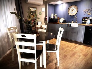 Un coin repas avec une table ronde et des chaises blanches, une cuisine avec une horloge et une décoration sur le th ème du café, et un plancher en bois.