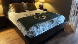 Una cama bien hecha con una colcha estampada con motivos florales, una lámpara de noche y una pequeña planta en la mesita.