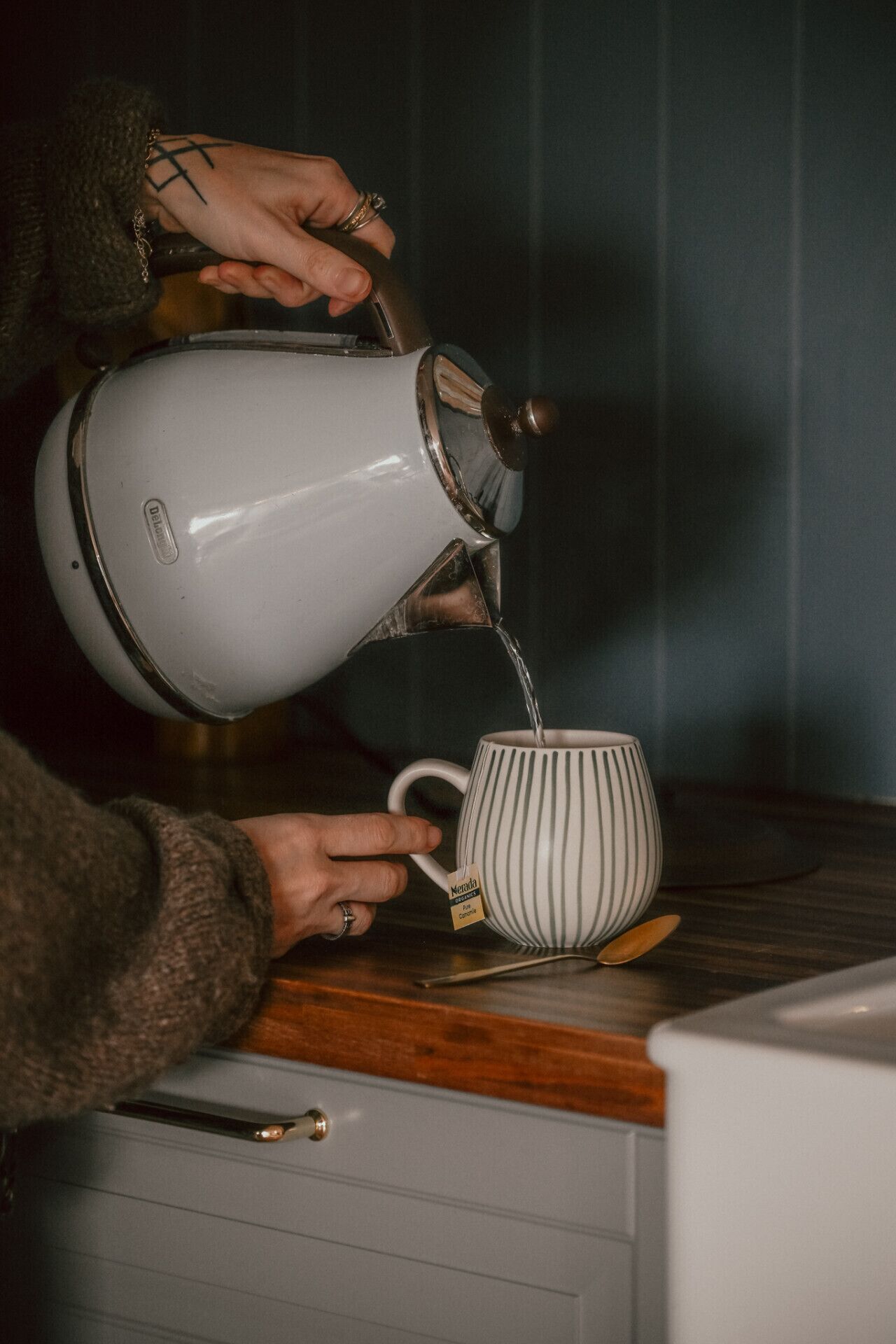 Una persona vertiendo líquido de un hervidor en una taza a rayas.