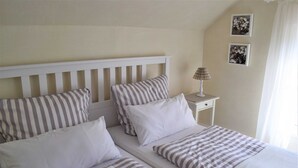 A double bed with striped bedding, a white headboard, and a bedside table with a lamp. - Ferienwohnung Andresen - FW Andresen (Pommerby)