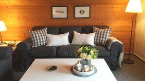A room with a wooden wall, a sofa with checkered pillows, a coffee table with a vase and candles, and framed pictures on the wall. - Ferienwohnung Andresen - FW Andresen (Pommerby)
