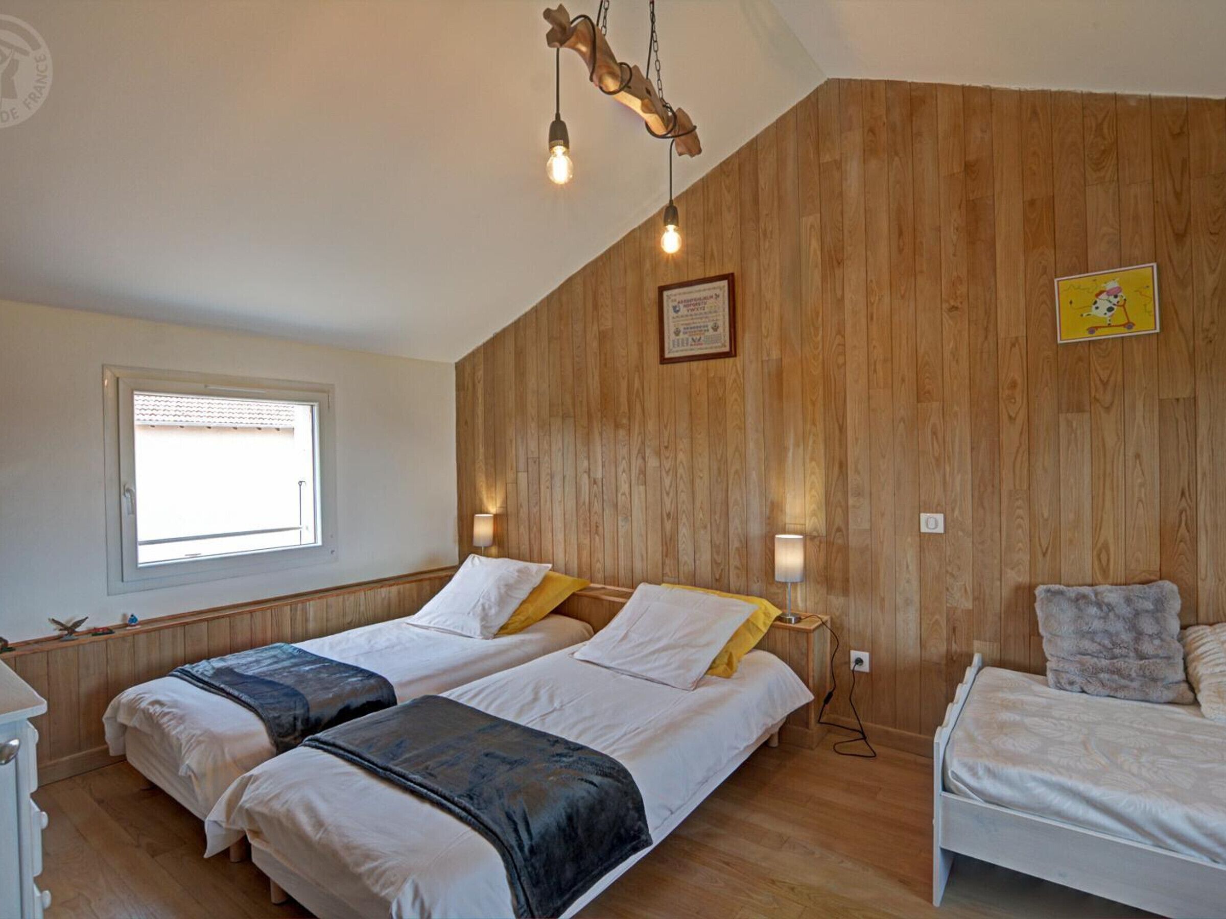 Een kamer met twee bedden, houten lambrisering, een raam en een ingelijst certificaat aan de muur.
