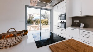 Cocina moderna con armarios blancos, encimera negra y un amplio ventanal con vistas a un jardín.