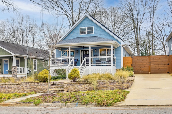 A two-story house with a porch, a stone retaining wall, and a wooden fence.