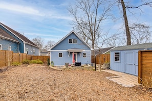 A residential backyard with a blue house, a wooden fence, and a shed.