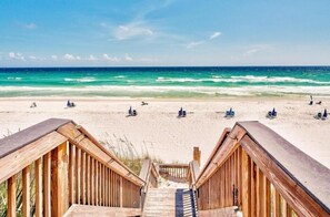 Een houten trap die naar een zandstrand met helderblauw water leidt.