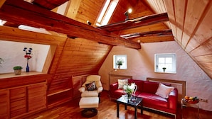 Une pièce mansardée chaleureuse avec des poutres en bois, un canapé rouge, une petite table et une fenêtre agrémentée d’une plante.