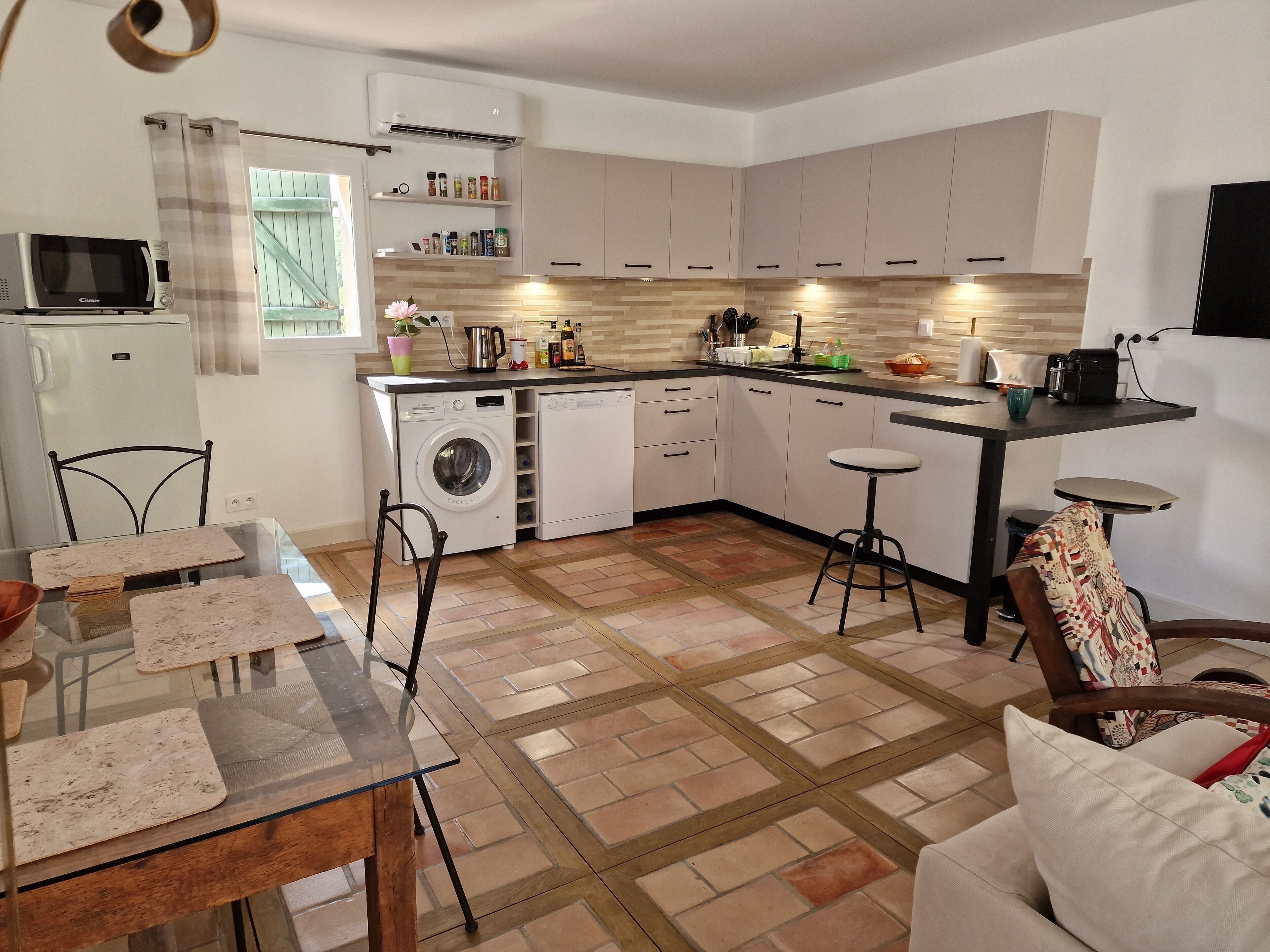 Une cuisine moderne équipée d’un lave-linge, d’un four à micro-ondes et d’un coin repas avec une table et des chaises en verre.