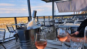 Een restaurant met terras aan het water, met metalen stoelen, tafels en een grote metalen container.