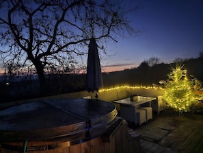 Un espace avec un jacuzzi, une terrasse en bois, du mobilier d’extérieur et des guirlandes lumineuses.