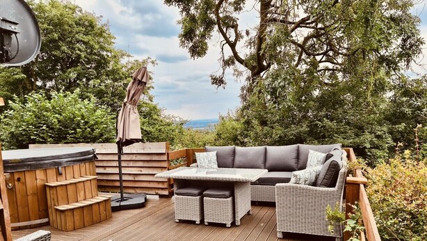 A wooden deck with a hot tub, wicker furniture, and a view of the surrounding greenery.