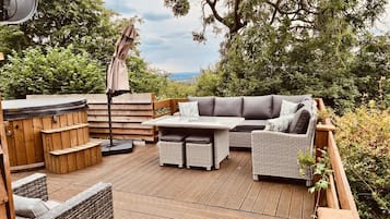 A wooden deck with a hot tub, wicker furniture, and a view of the surrounding greenery.