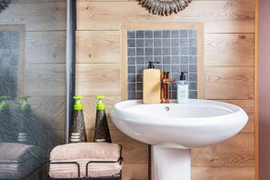 Une salle de bain avec un mur en bois, un lavabo blanc et deux distributeurs de savon liquide verts.