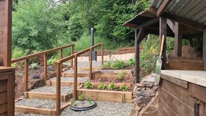 A wooden deck with steps leading to a garden area, surrounded by trees.