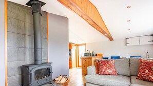 A cozy living room with a stone fireplace, a grey sofa, and a kitchen in the background.