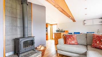 A cozy living room with a stone fireplace, a grey sofa, and a kitchen in the background.