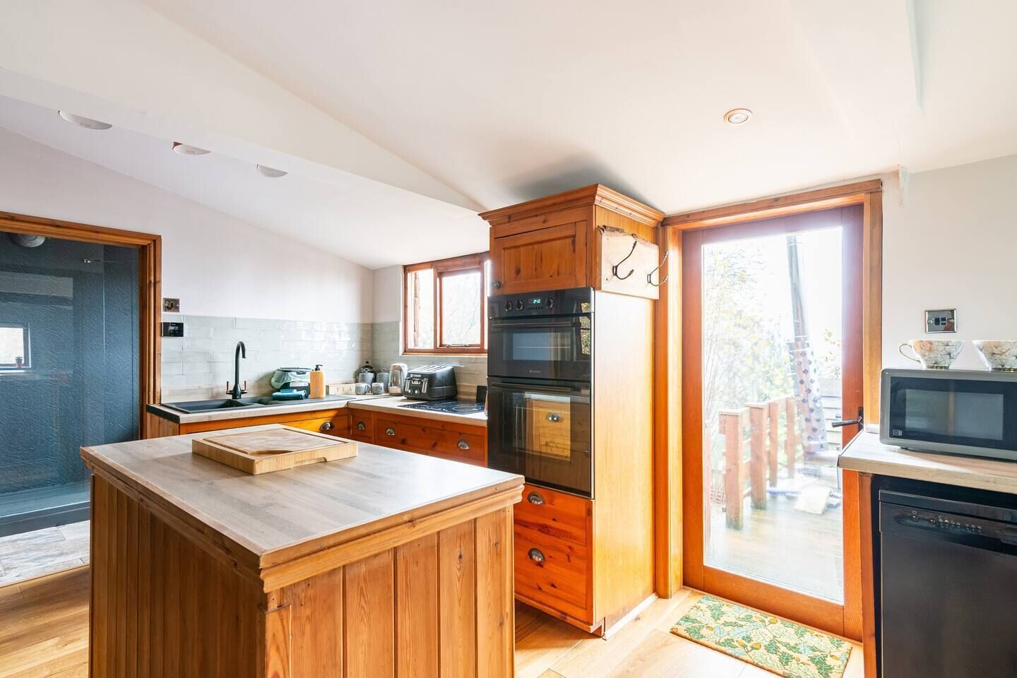 Une cuisine moderne avec des meubles en bois, un îlot central, un four encastré et un four à micro-ondes.
