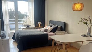 Ein modernes Schlafzimmer mit Bett, Nachttisch, Lampe und Blick ins Freie.